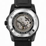 A close-up shot of a wristwatch showing its open back case with a black dial and black strap, revealing a silver stainless steel case back with a visible mechanical movement.
